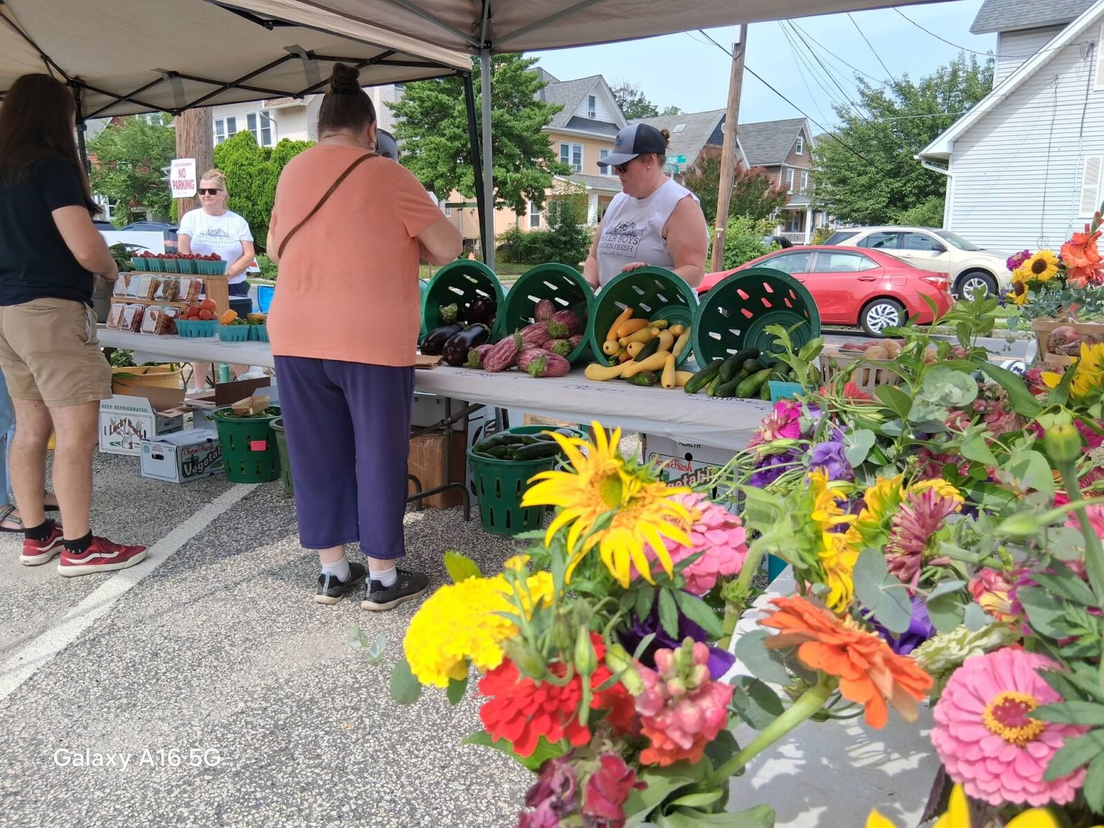 Fresh Produce Flowers Farm Market Stand Baskets of eggplant, squash and cucumbers on a market table with cut flowers in the foreground.