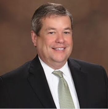 Gerald Oconnor Headshot Gerald O'Connor smiles in a dark suit and light green tie against a brown backdrop.