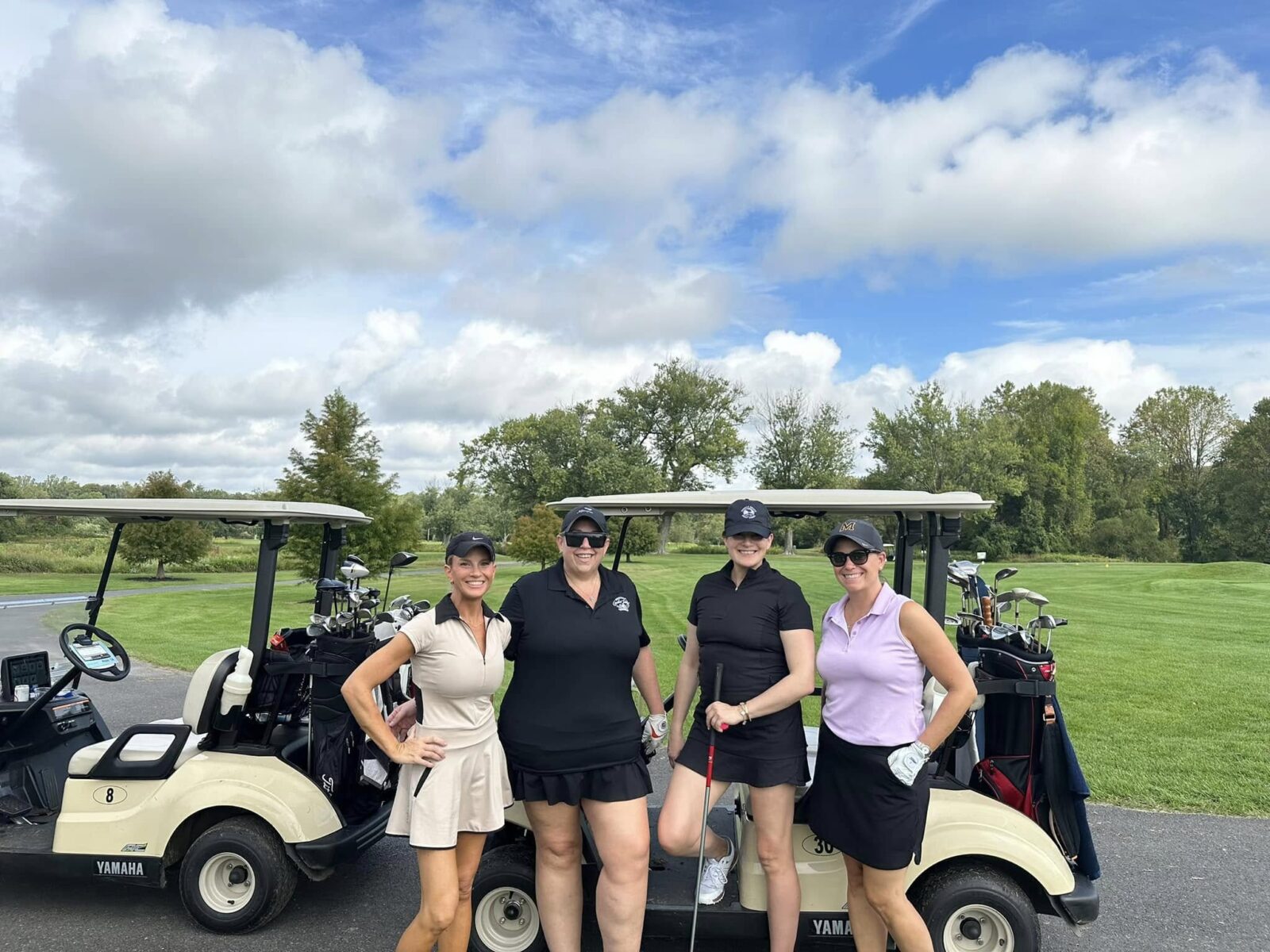 Golf Outing Golfers Main Street Woodbury Four women in golf attire stand between two golf carts on a fairway path.