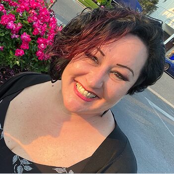 Jennifer Maurer Headshot Jennifer Maurer smiles outdoors in a black top with pink flowers blooming behind her.