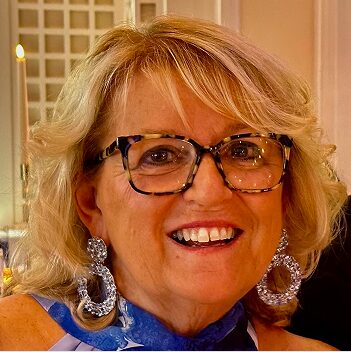 Mary Carter Headshot Mary Carter smiles wearing tortoiseshell glasses and large statement earrings.