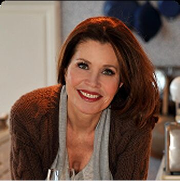 Peg Sickel Headshot Peg Sickel smiles in a brown cardigan and grey scarf in a bright kitchen.